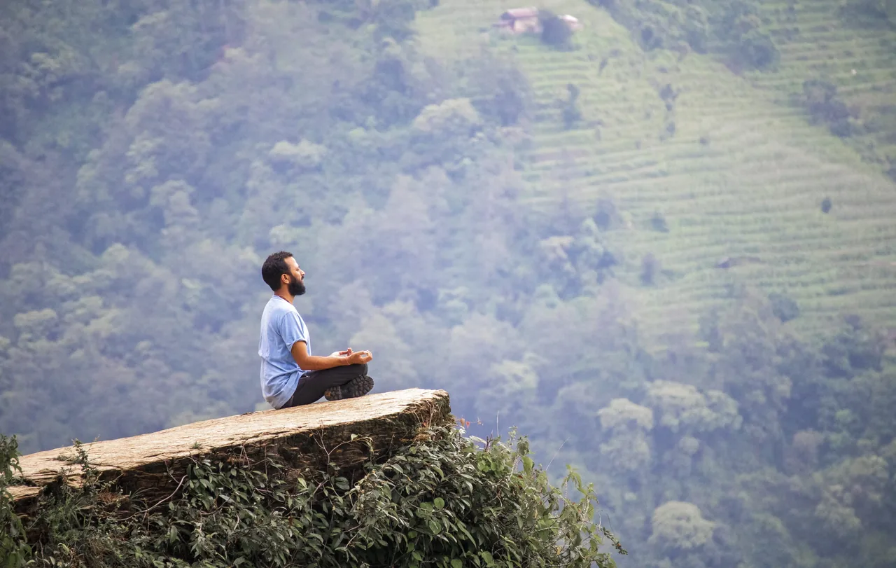 Meditator seated on a cliff edge overlooking the valley